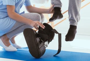 Close up of Helpful professional physiotherapist helps the patient to put on an orthosis for the first time